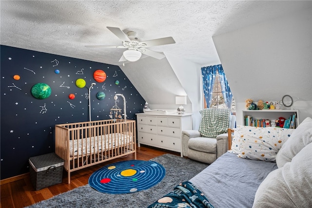 bedroom featuring a ceiling fan, an accent wall, dark wood-type flooring, vaulted ceiling, and a textured ceiling