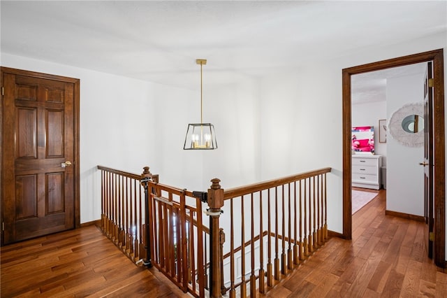 hallway featuring baseboards, dark wood finished floors, a notable chandelier, and an upstairs landing