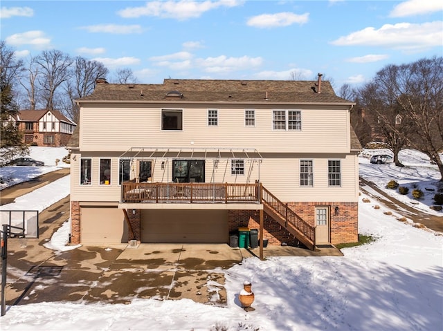 snow covered house with brick siding, stairway, an attached garage, and a wooden deck