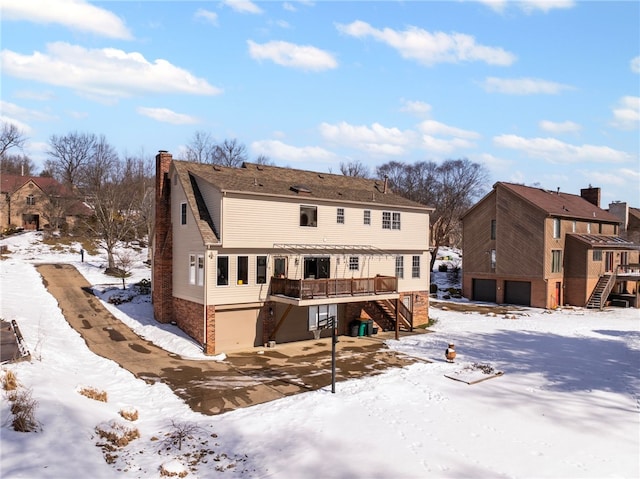 snow covered house with an attached garage, stairs, a chimney, and a deck