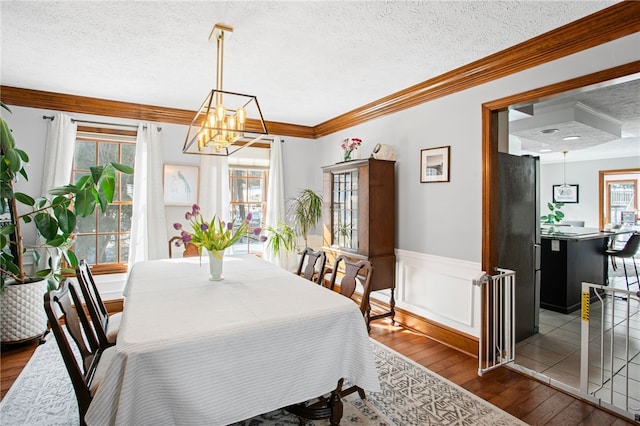 dining room featuring a wainscoted wall, crown molding, a notable chandelier, a textured ceiling, and wood finished floors