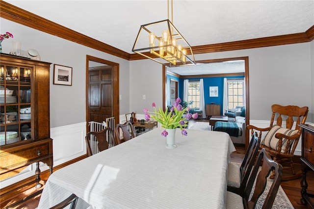 dining space featuring crown molding, a chandelier, wood finished floors, and wainscoting