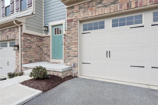 view of exterior entry with a garage, stone siding, and driveway