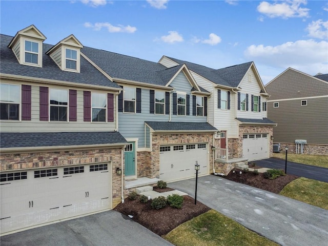 townhome / multi-family property featuring a garage, stone siding, roof with shingles, and driveway