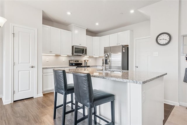 kitchen with appliances with stainless steel finishes, white cabinetry, and a center island with sink