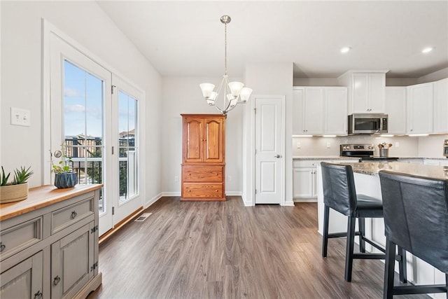 kitchen with appliances with stainless steel finishes, white cabinetry, hanging light fixtures, and dark wood-type flooring