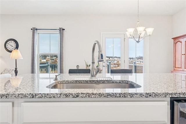 kitchen featuring light stone counters, decorative light fixtures, white cabinetry, a sink, and a chandelier