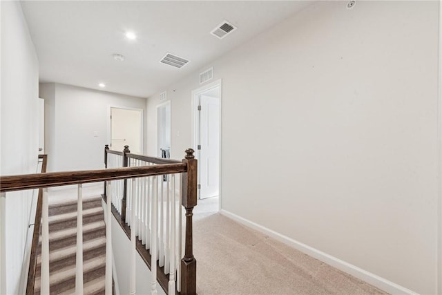 hallway with baseboards, visible vents, light carpet, and an upstairs landing