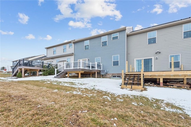 snow covered rear of property with a deck, a yard, and stairway