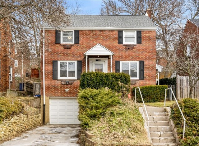 colonial-style house with a garage, driveway, brick siding, and a chimney