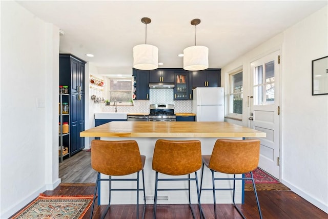 kitchen with a breakfast bar area, under cabinet range hood, stainless steel appliances, wood counters, and blue cabinetry