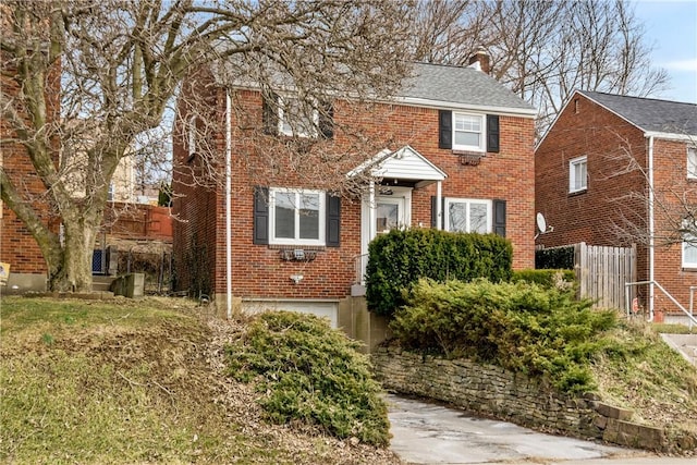 colonial-style house with an attached garage, a chimney, fence, and brick siding