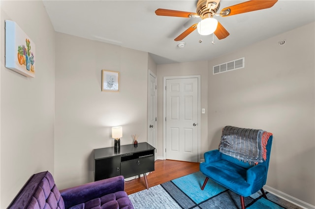 living area featuring a ceiling fan, wood finished floors, visible vents, and baseboards