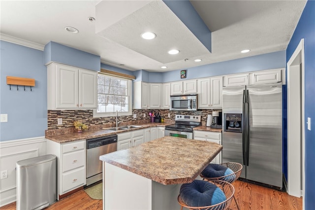 kitchen with light wood finished floors, appliances with stainless steel finishes, white cabinets, a kitchen island, and a sink