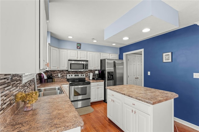 kitchen with stainless steel appliances, a sink, white cabinets, light countertops, and a center island