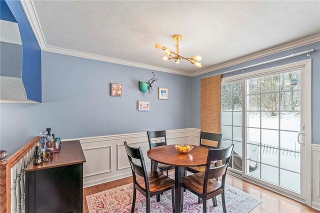 dining room with a wainscoted wall, wood finished floors, an inviting chandelier, crown molding, and a textured ceiling