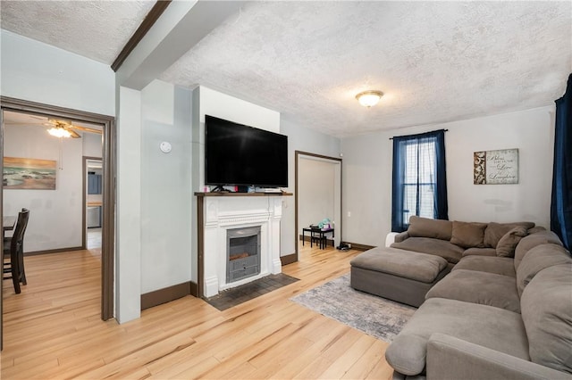 living room with a textured ceiling, light wood finished floors, a fireplace with flush hearth, and baseboards