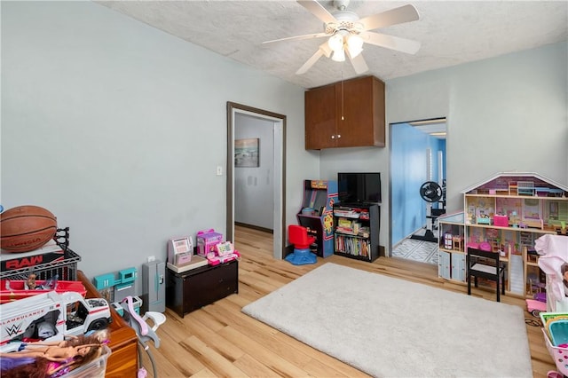 playroom featuring a textured ceiling, a ceiling fan, and light wood-style floors