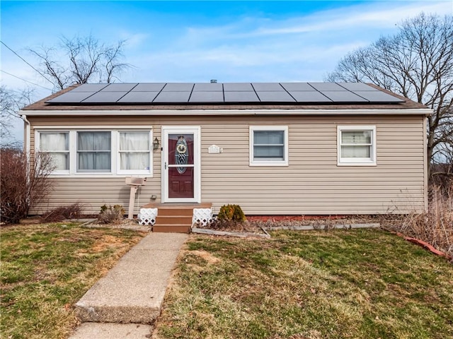 bungalow-style house featuring entry steps, a front lawn, and solar panels