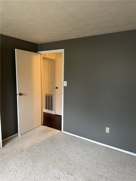 spare room featuring carpet floors, visible vents, a textured ceiling, and baseboards