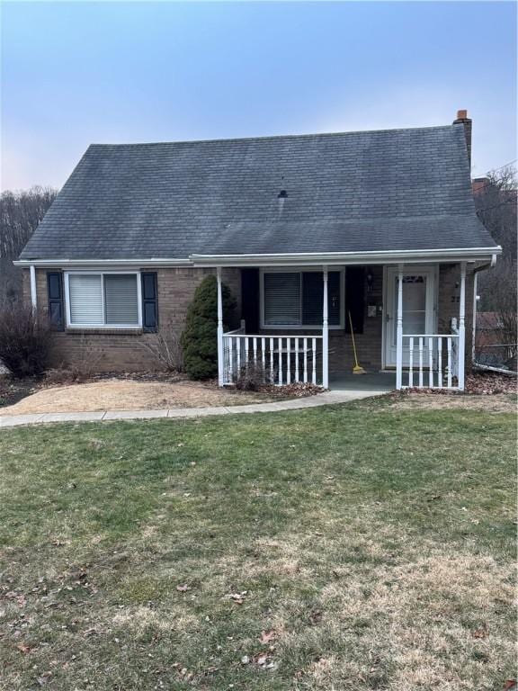 view of front of home featuring covered porch, brick siding, a front lawn, and a shingled roof