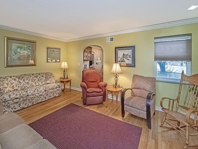 living area featuring arched walkways, wood finished floors, visible vents, baseboards, and ornamental molding