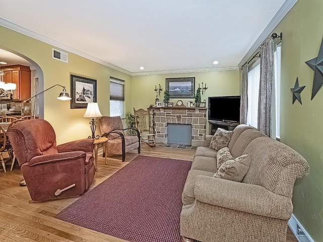 living area with arched walkways, a fireplace, visible vents, light wood-type flooring, and crown molding