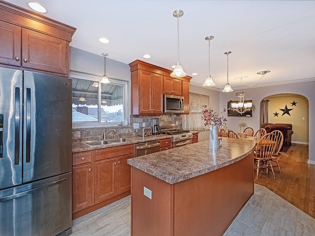 kitchen featuring a center island, arched walkways, decorative light fixtures, stainless steel appliances, and a sink