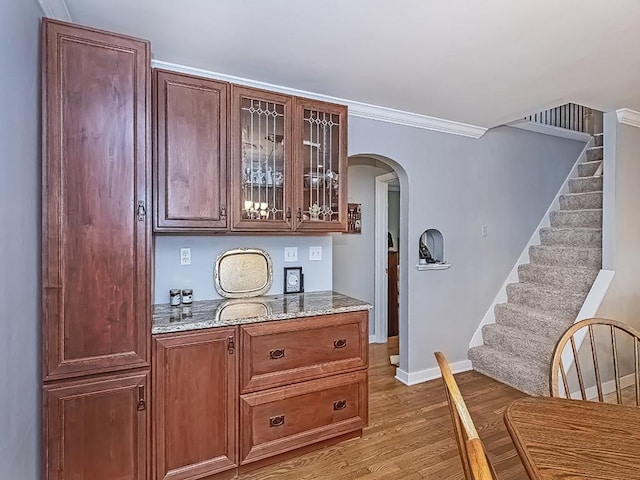 bar featuring arched walkways, stairway, ornamental molding, wood finished floors, and baseboards