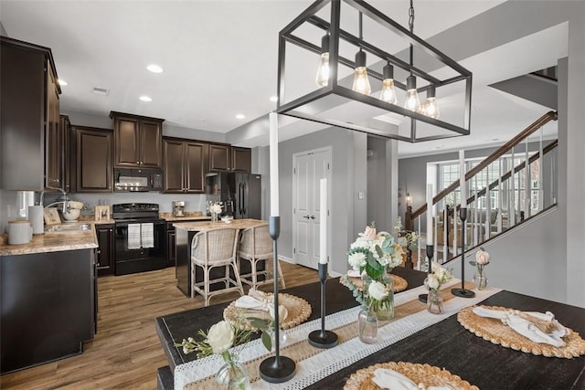 kitchen with a kitchen island, wood finished floors, dark brown cabinets, black appliances, and a kitchen bar