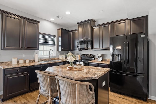 kitchen with light wood finished floors, visible vents, a kitchen island, black appliances, and a sink