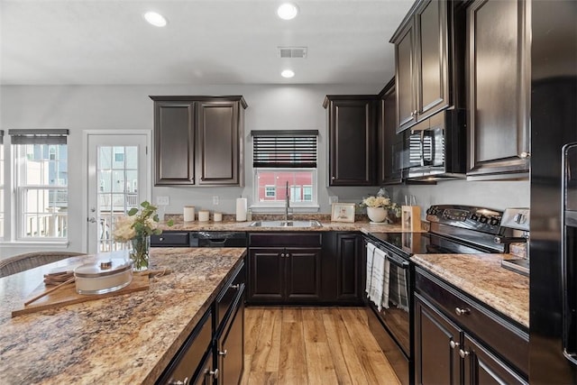 kitchen featuring visible vents, light wood-style flooring, light stone counters, black range with electric cooktop, and a sink