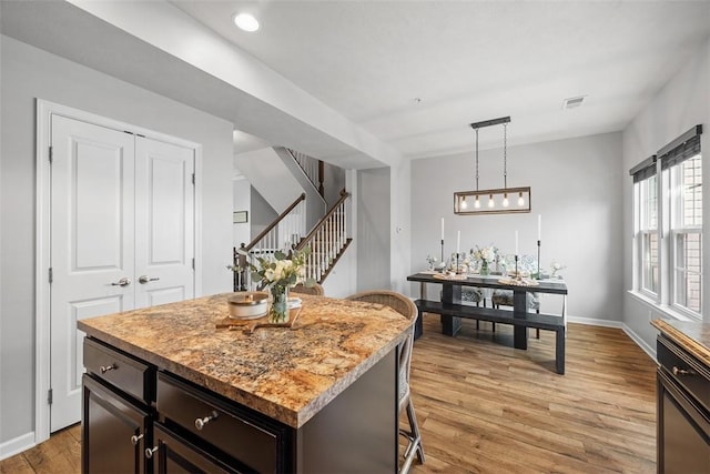 kitchen featuring decorative light fixtures, visible vents, light wood-style flooring, a kitchen island, and baseboards