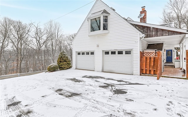 view of snowy exterior with a chimney and an attached garage