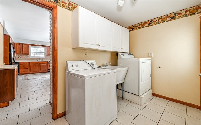 clothes washing area featuring light tile patterned floors, cabinet space, washing machine and dryer, a sink, and baseboards