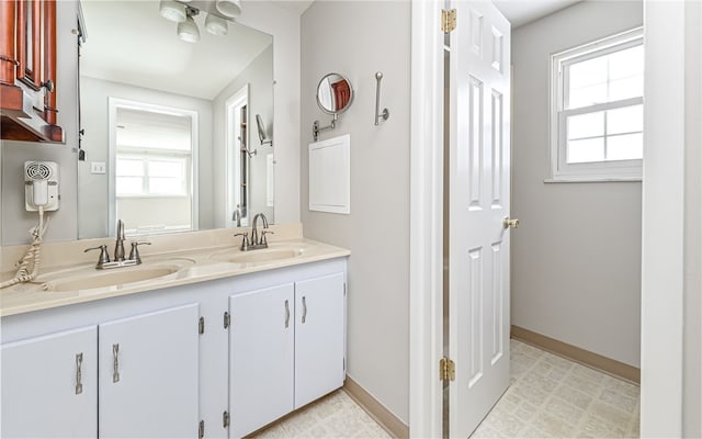 full bath with double vanity, a sink, and baseboards