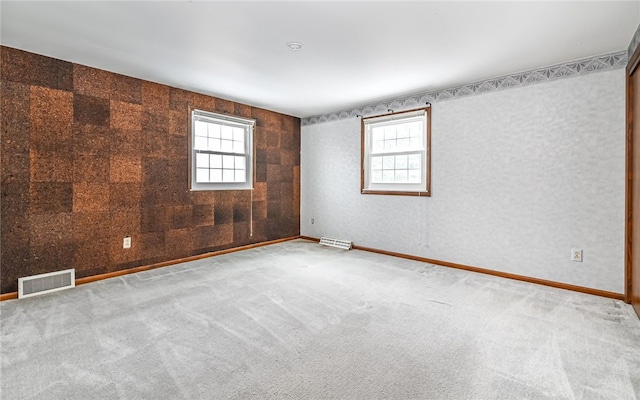 carpeted empty room featuring a wealth of natural light, visible vents, and baseboards