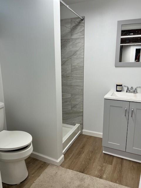 bathroom featuring a stall shower, baseboards, toilet, wood finished floors, and vanity