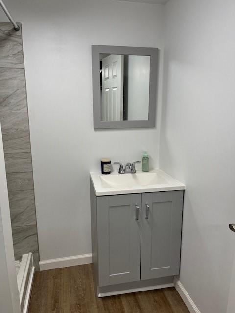 full bathroom featuring tiled shower, vanity, baseboards, and wood finished floors