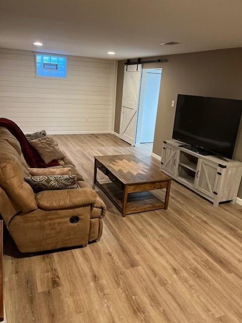 living area featuring light wood-type flooring, a barn door, and baseboards