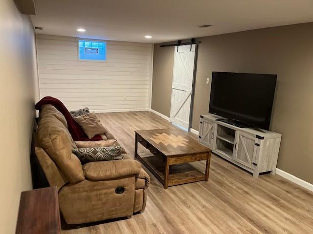 living room with light wood finished floors, a barn door, visible vents, baseboards, and recessed lighting