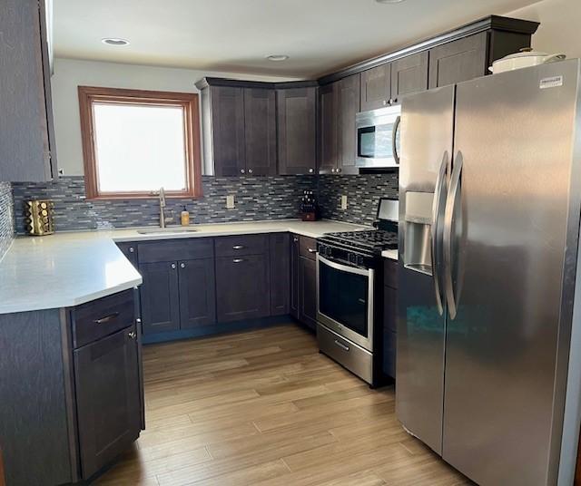 kitchen with decorative backsplash, light wood-style flooring, appliances with stainless steel finishes, light countertops, and a sink