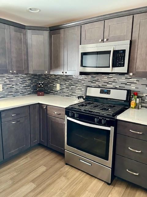 kitchen featuring stainless steel appliances, light countertops, dark brown cabinetry, and light wood-style flooring