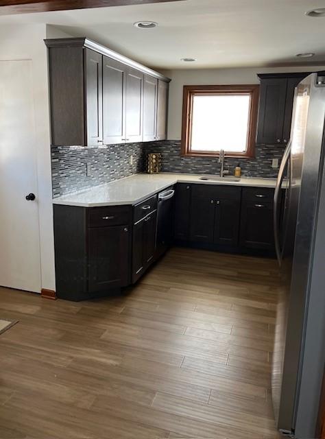 kitchen featuring light countertops, decorative backsplash, appliances with stainless steel finishes, light wood-style floors, and a sink