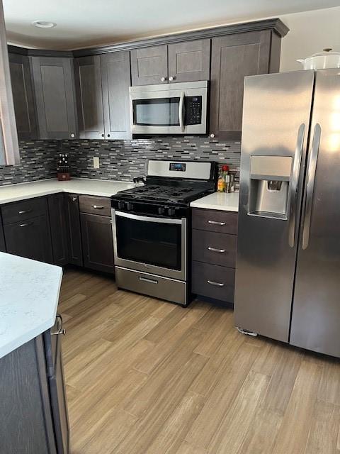 kitchen with stainless steel appliances, dark brown cabinets, light countertops, and light wood-style floors