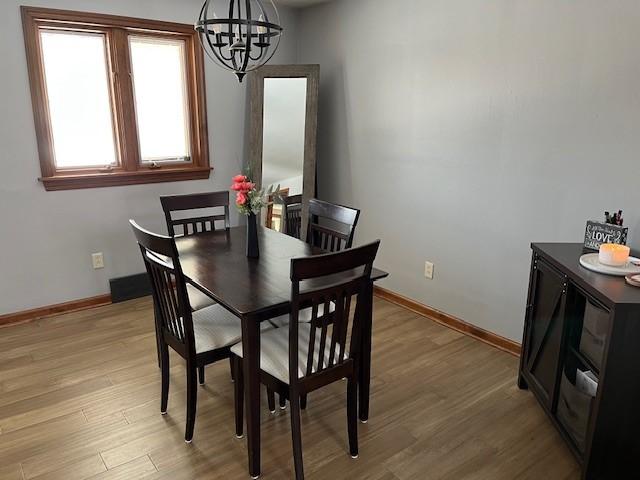 dining area with light wood-type flooring, baseboards, and an inviting chandelier