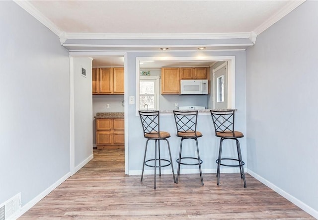 kitchen featuring visible vents, white microwave, a kitchen breakfast bar, light wood-type flooring, and baseboards