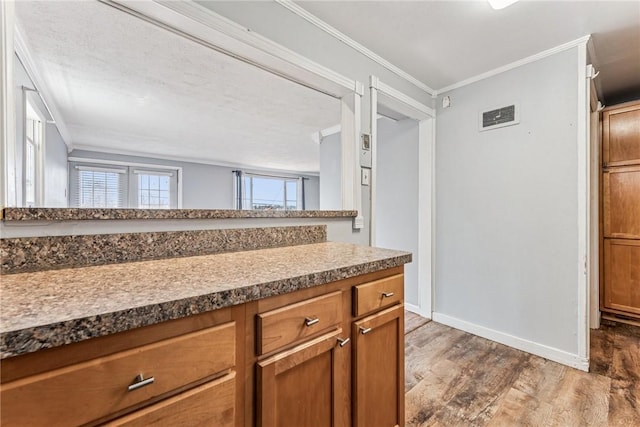 kitchen featuring dark wood-style flooring, brown cabinets, visible vents, ornamental molding, and baseboards