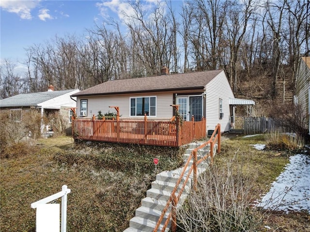 ranch-style house featuring a deck, a shingled roof, and fence