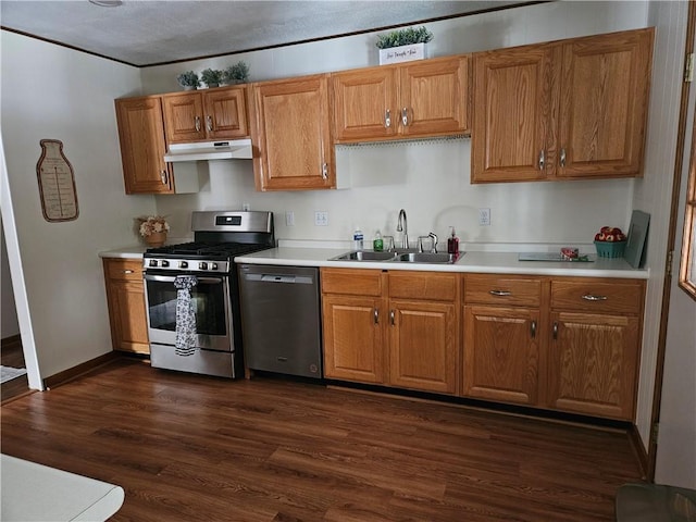 kitchen with a sink, under cabinet range hood, light countertops, appliances with stainless steel finishes, and dark wood-style flooring